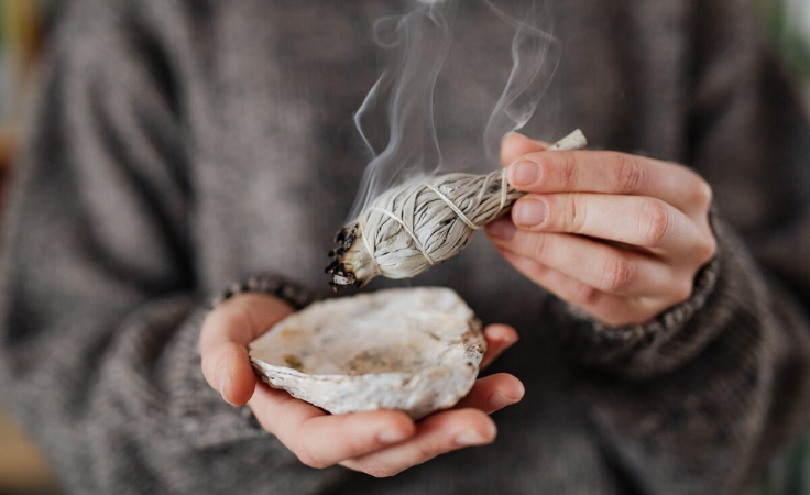 a biohacker holds the burning sage to remove the negative energy from home
